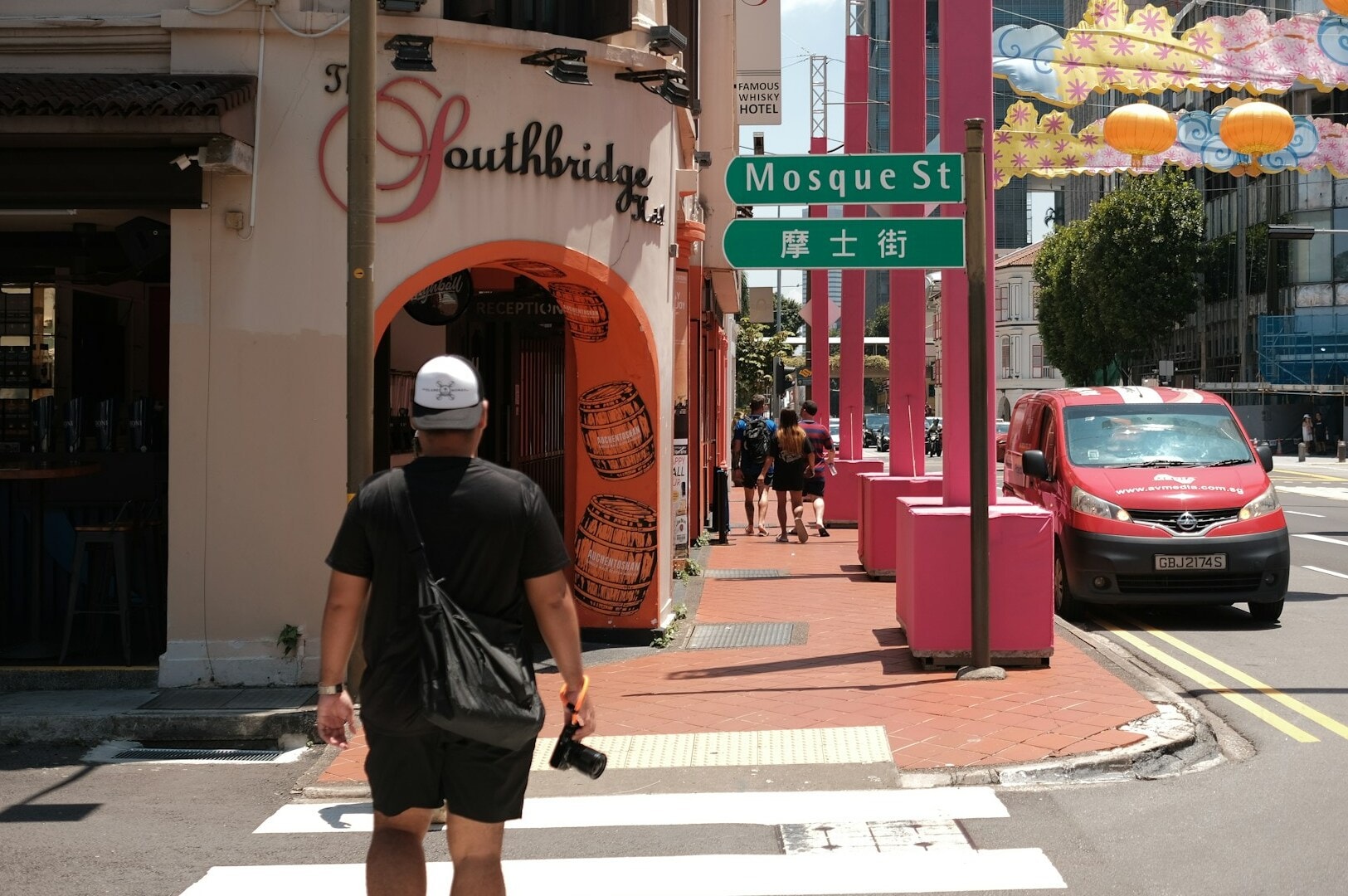 A man strolls through a lively Singapore Hawker Centre, with colorful food stalls lining the street.