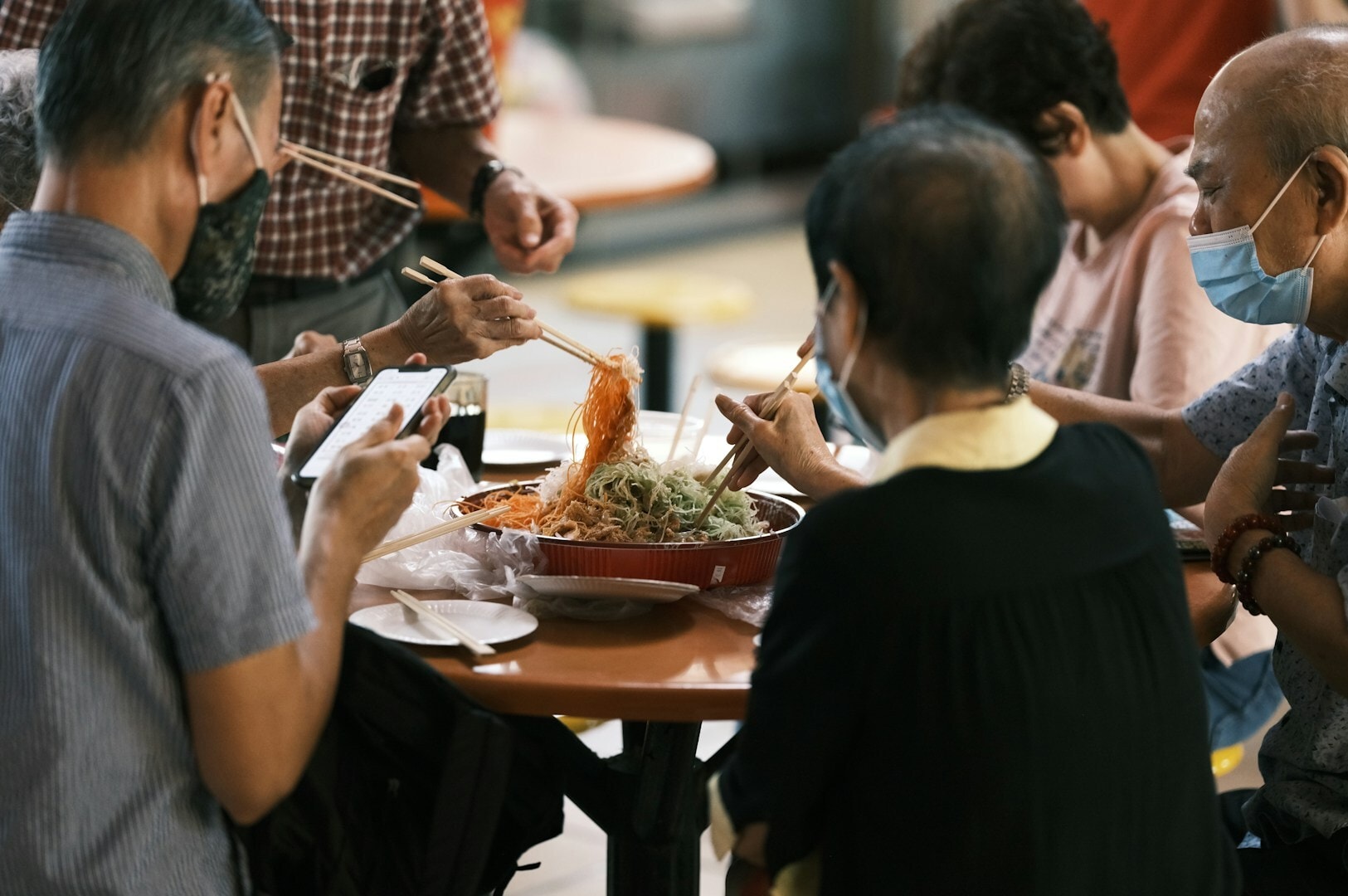 A group of people sharing a meal at a table filled with diverse food in a lively Singapore Hawker Centre.