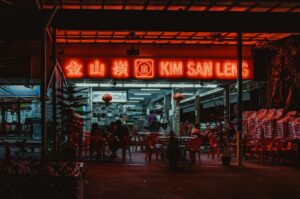 Bright neon sign in a bustling Singapore Hawker Centre.