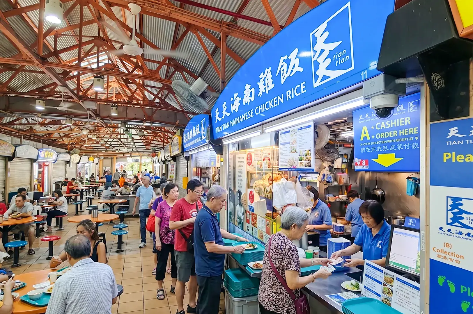 A busy queue of customers at the famous Tian Tian Hainanese Chicken Rice stall inside Maxwell Food Centre, Singapore, showing the vibrant atmosphere of a traditional hawker centre.