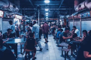 A lively food court in Singapore, showcasing diverse diners eating and drinking amidst a vibrant atmosphere.
