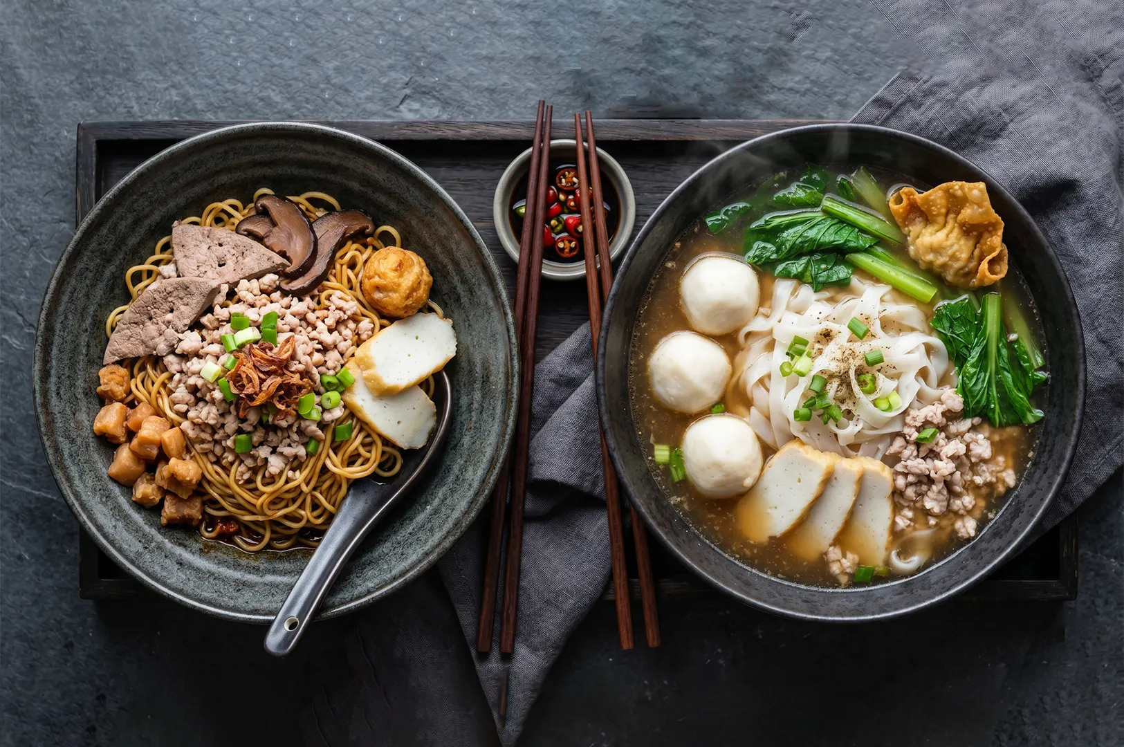 Singaporean dry Bak Chor Mee on the left with minced pork and pork liver, next to a bowl of fishball noodle soup on the right.