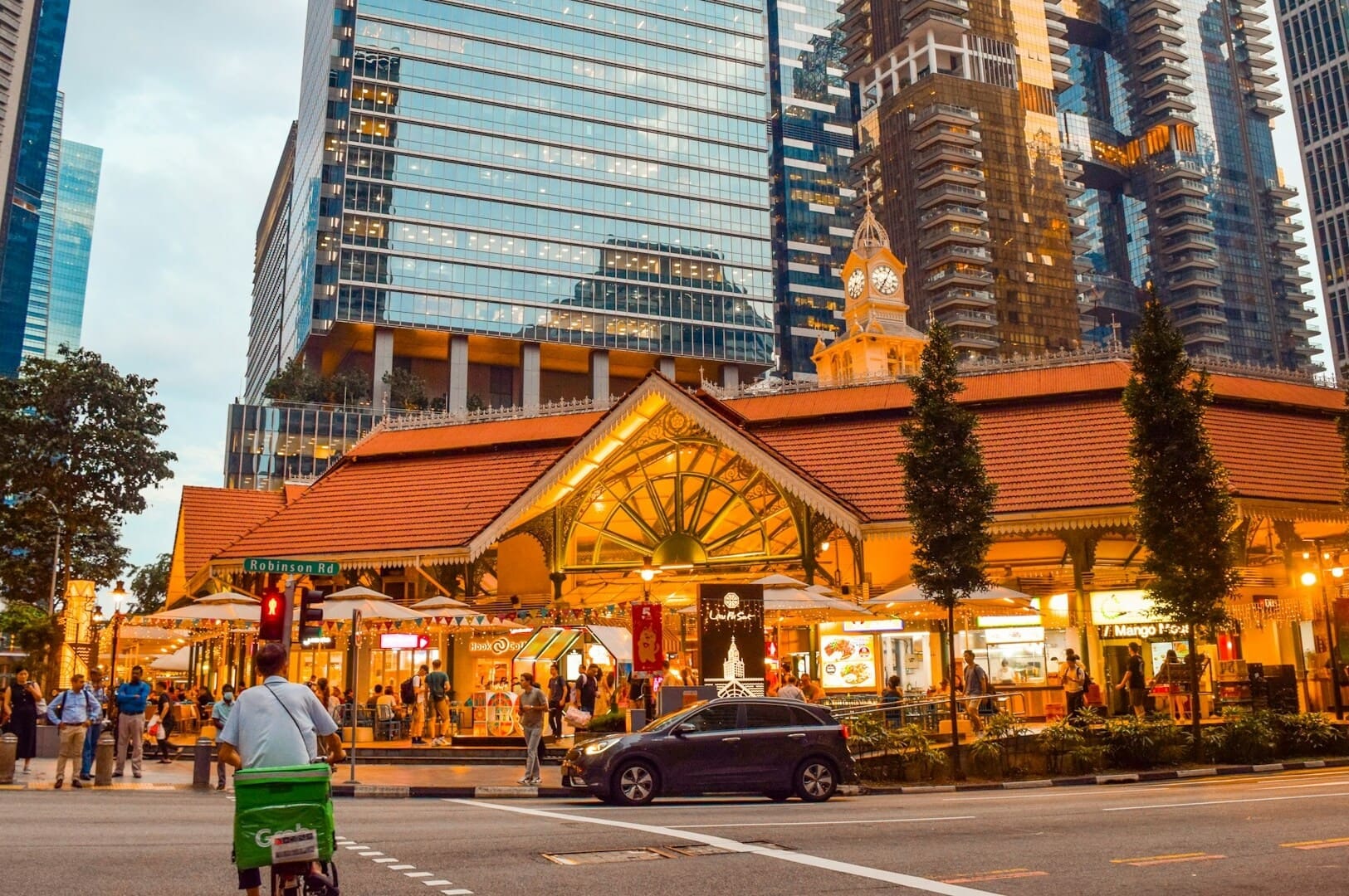  A man on a scooter navigating a city street, with a Singapore Hawker Centre visible in the background.