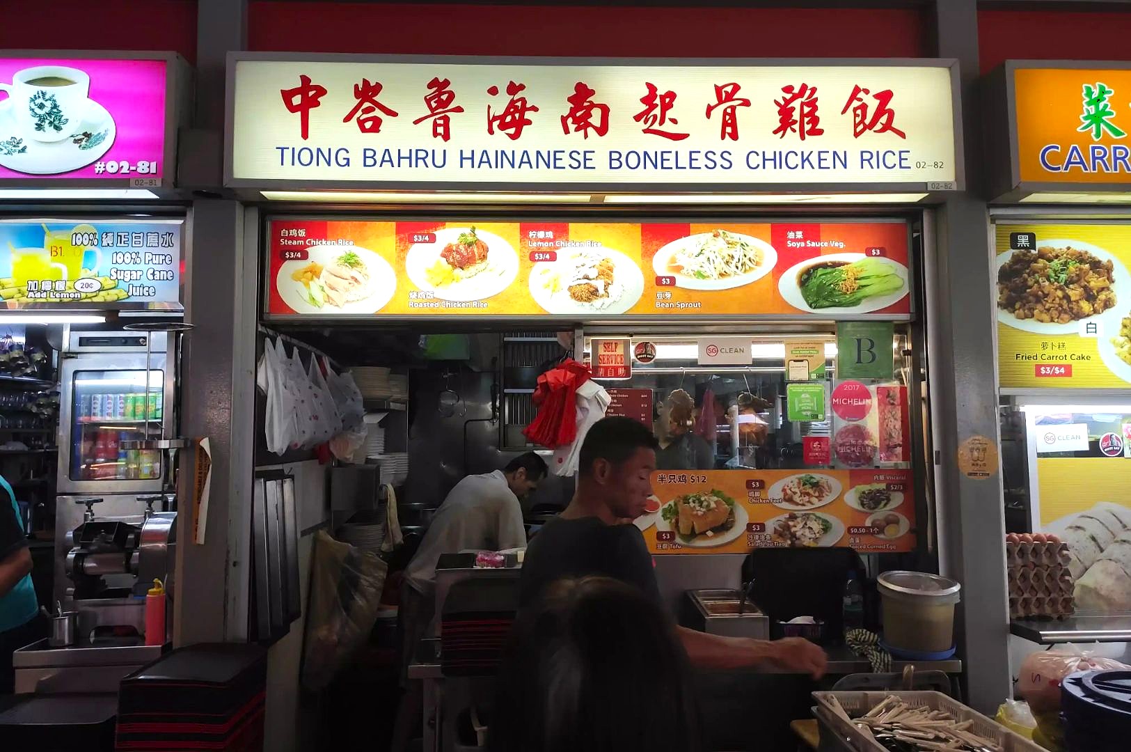 Hawker stall with a sign reading "Tiong Bahru Hainanese Boneless Chicken Rice" in red. Menu displays chicken rice dishes. Busy food preparation scene.