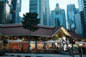 A vibrant Singapore street scene showcasing a hawker centre restaurant alongside a parked car.