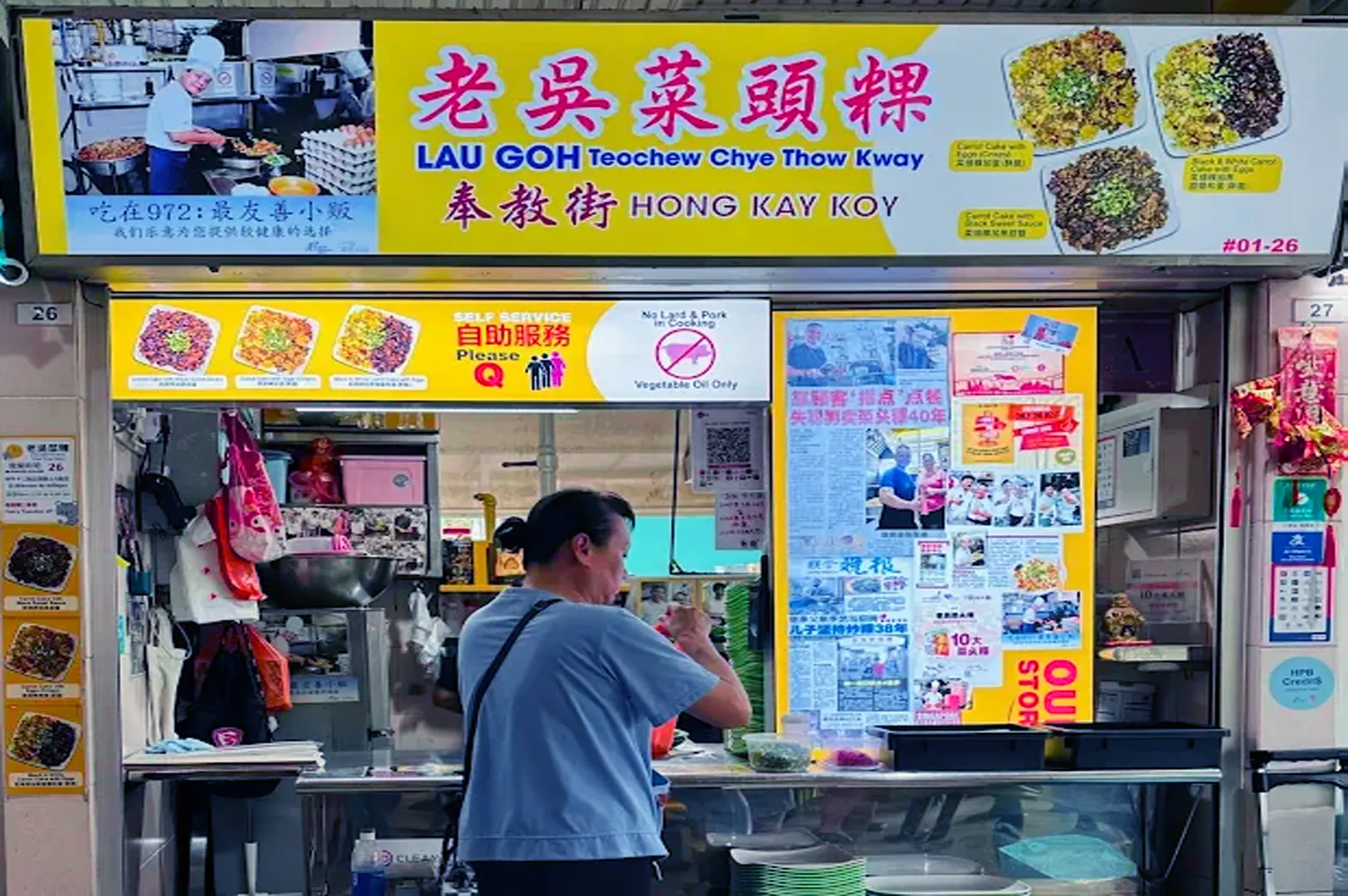 A woman stands at a vibrant food stall labeled "Lau Goh Teochew Chye Thow Kway." The counter displays colorful dishes, with the cheerful atmosphere suggesting a popular local eatery.