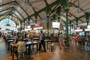 The vibrant food court of a Singapore hawker centre, showcasing numerous stalls with a variety of local dishes.