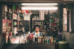 A woman stands in front of a Singapore hawker store, showcasing the vibrant local food culture.