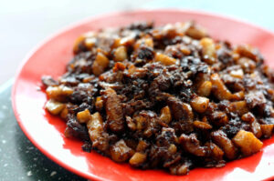 A dish of meat and onions served on a plate, with a piece of Black Carrot Cake beside it.