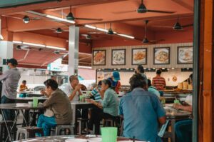 People seated at tables, savoring food in a lively Singapore hawker stall atmosphere.