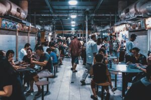 A lively food court in Singapore, showcasing diverse diners eating and drinking amidst a vibrant atmosphere.
