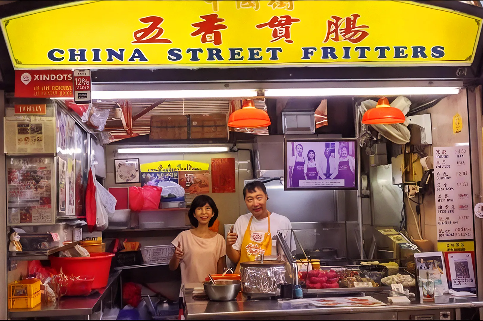 Couple smiling at a vibrant food stall, "China Street Fritters," with colorful signs and fritters displayed. Warm lighting creates a welcoming atmosphere.
