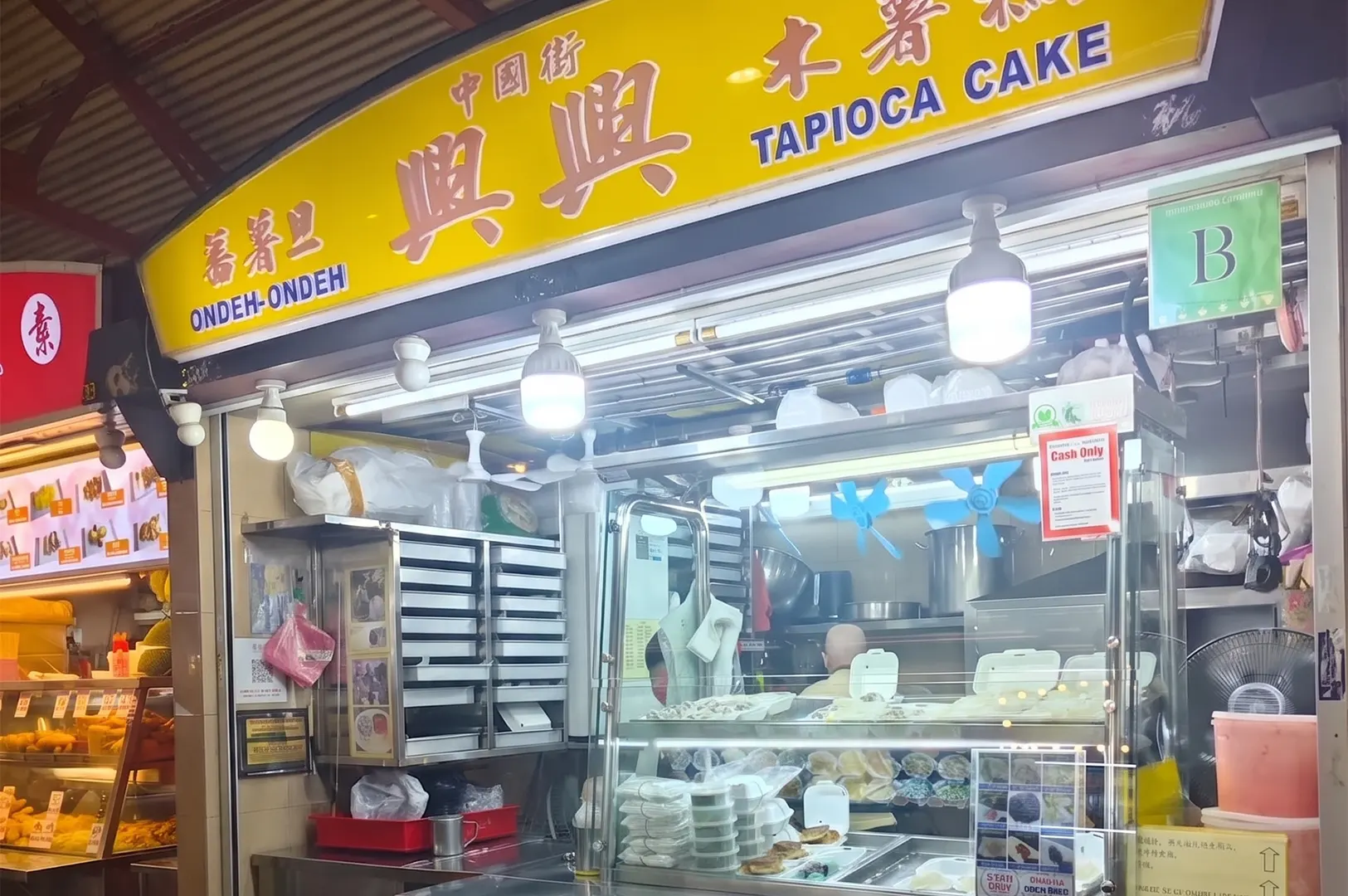 Xing Xing Ondeh-Ondeh and Tapioca Cake hawker stall storefront with a bright yellow sign and food display counter.