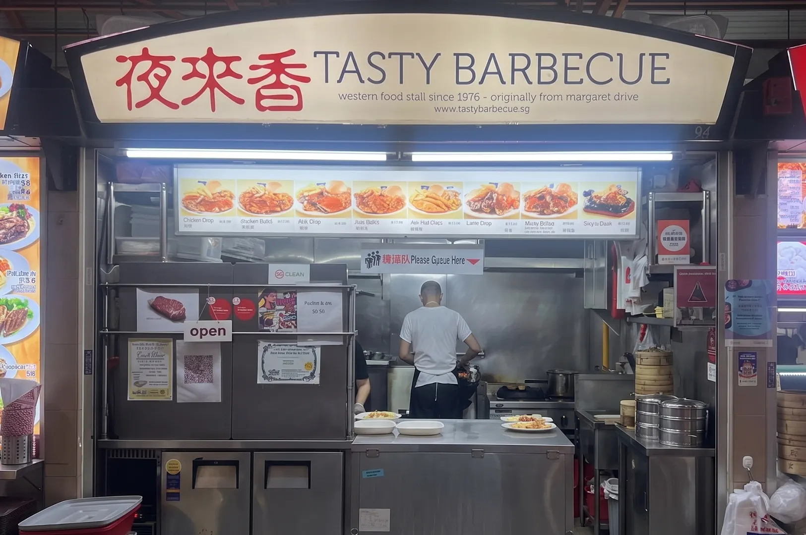 Tasty Barbecue hawker stall storefront displaying a Western food menu with plates prepared on the service counter.