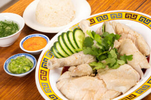 A table setting with a plate of Hainanese Chicken Rice, showcasing succulent chicken and fragrant rice.