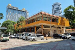 Front view of the yellow Golden Mile Food Centre, or Little Thailand, featuring parked cars in the foreground. Photo by Google.