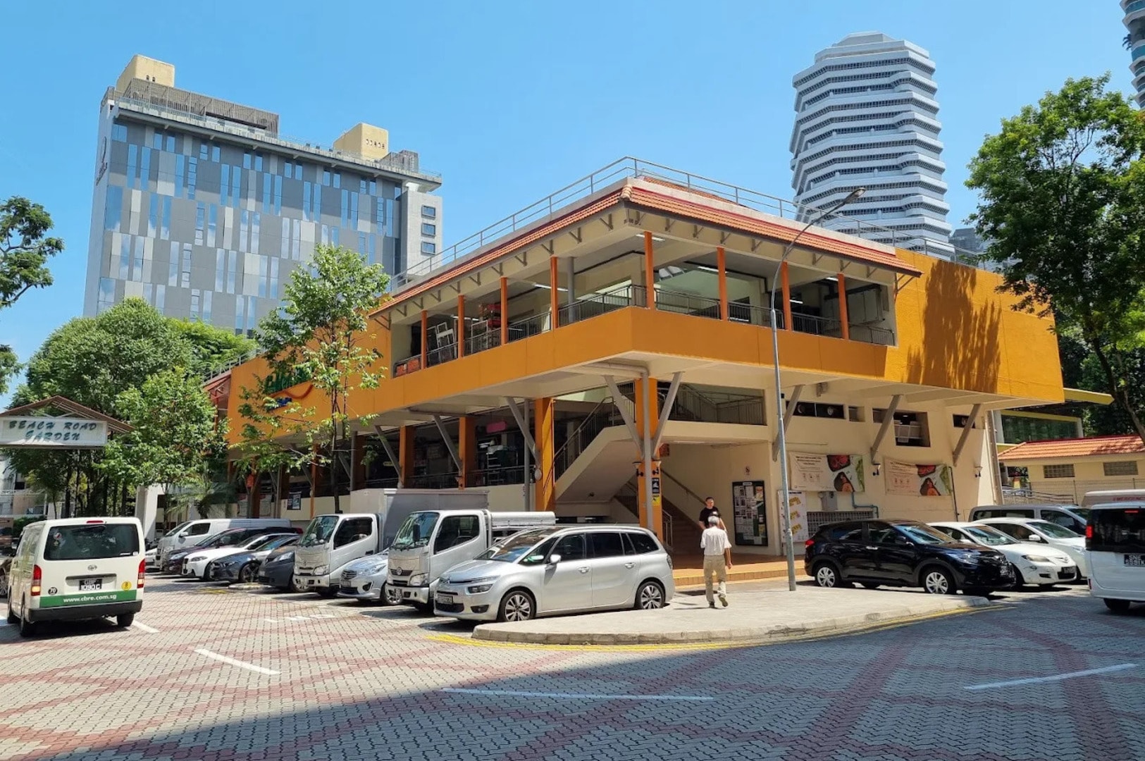 Front view of the yellow Golden Mile Food Centre, or Little Thailand, featuring parked cars in the foreground. Photo by Google.