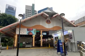Daytime view of a food court entrance with a large roof, set against a background of tall city buildings.