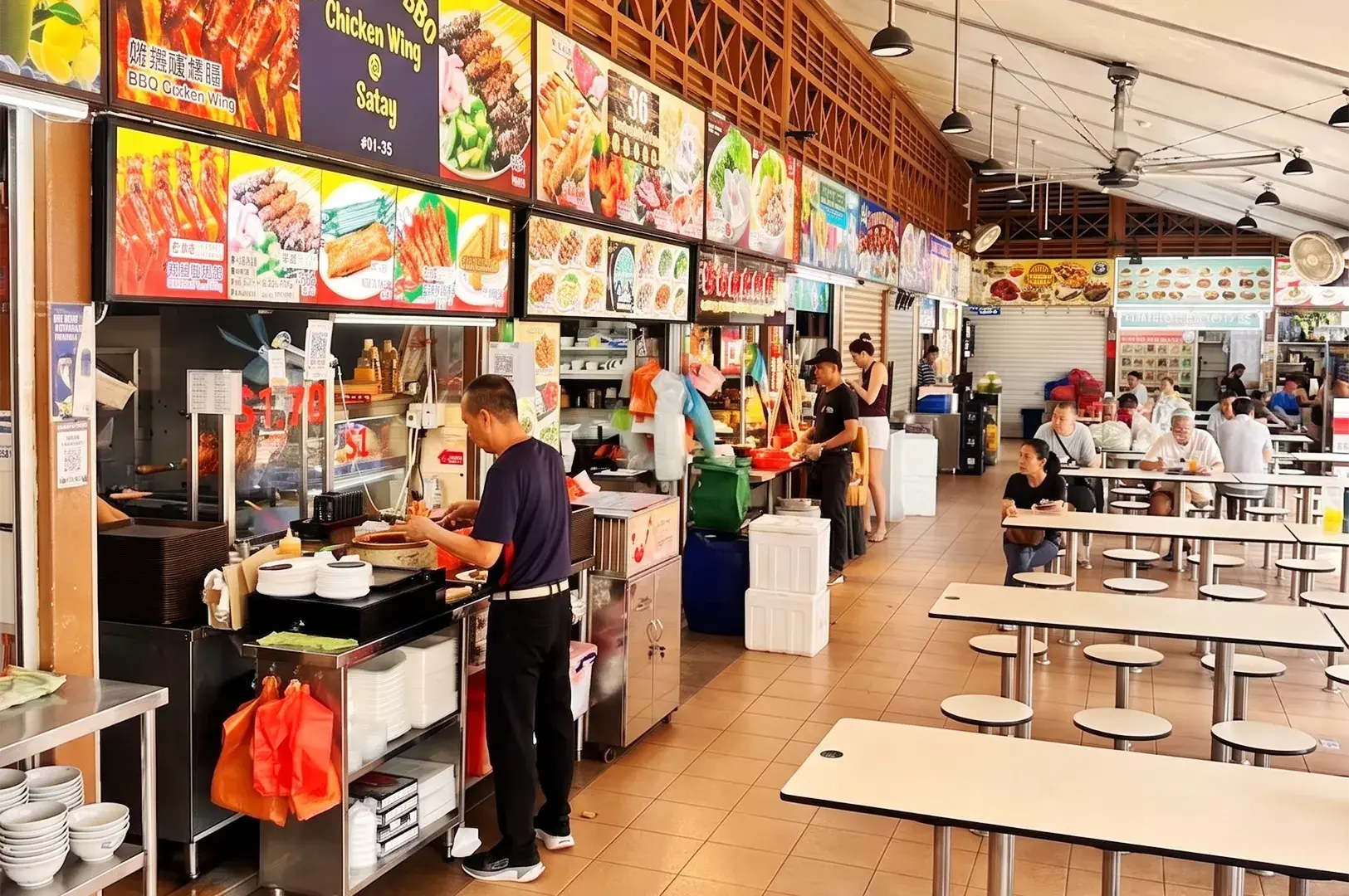 Busy indoor hawker center in Singapore featuring food stalls and a large seating area with tables and stools.