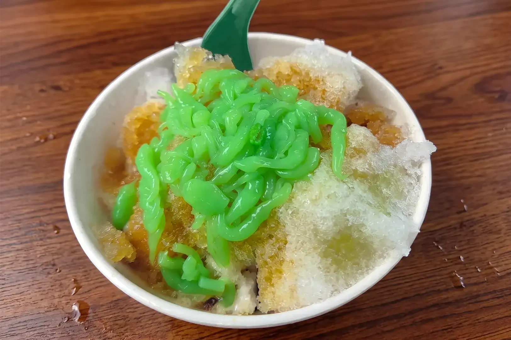 A bowl of Chendol from 88 San Ren Cold, topped with green pandan jelly noodles and shaved ice drizzled with gula melaka syrup.