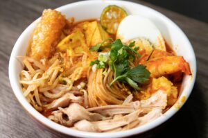 A vibrant bowl of Laksa with noodles, tender meat, and a soft-boiled egg, served in Chinatown.