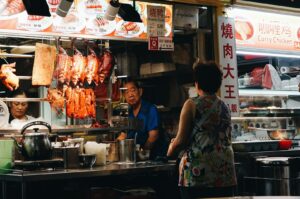 A woman poses in front of a food stand at Newton Food Centre, highlighting the vibrant food scene in Singapore.