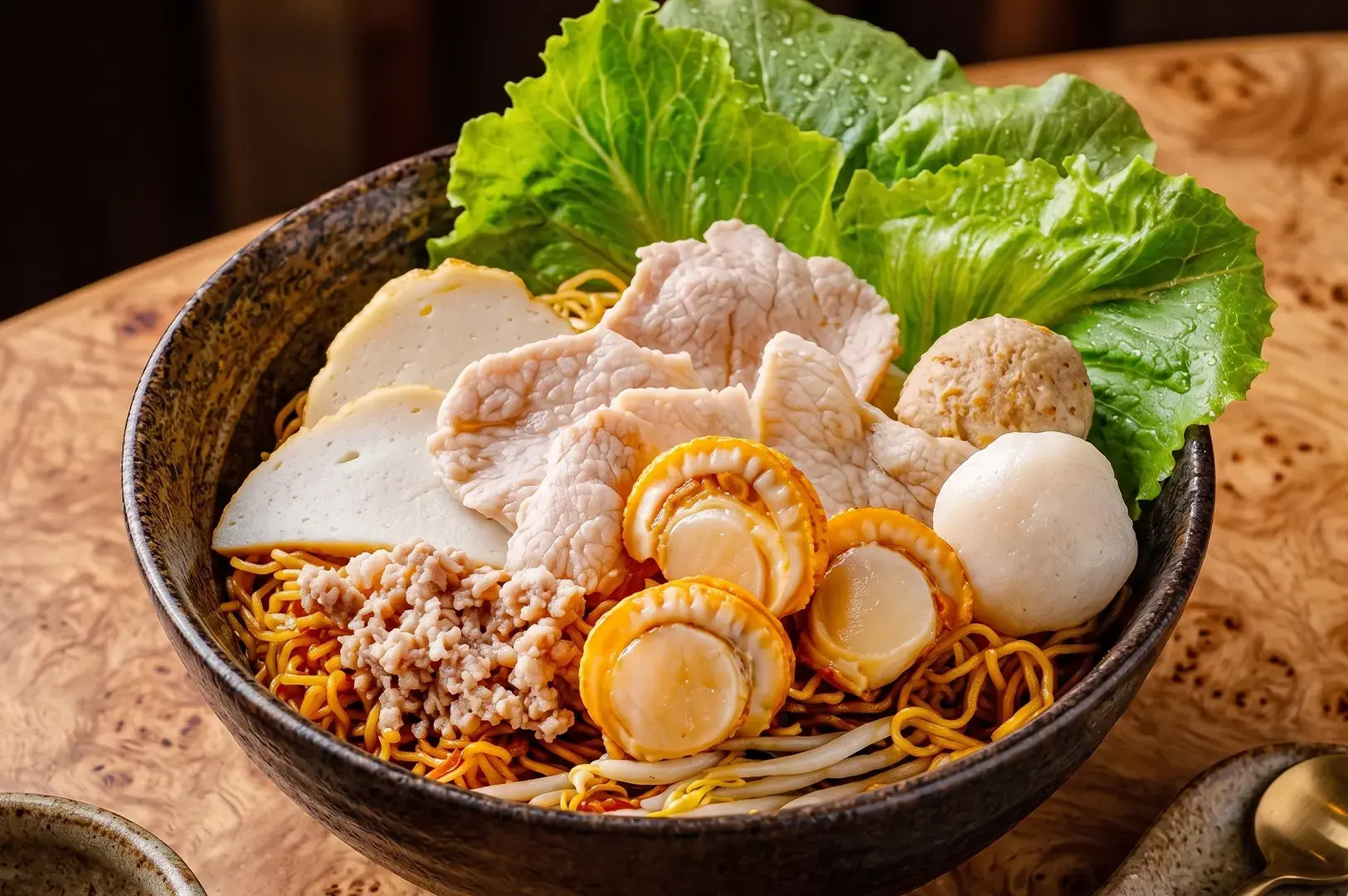 Bowl of dry noodles with scallops, sliced pork, fish cakes, meatballs, and lettuce.