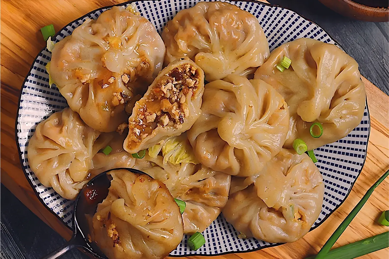 A plate of round dumplings with pleated edges, filled with a mixture of vegetables and nuts. One dumpling is cut open, displaying its contents. Fresh green onions garnish the dish, adding a touch of color.