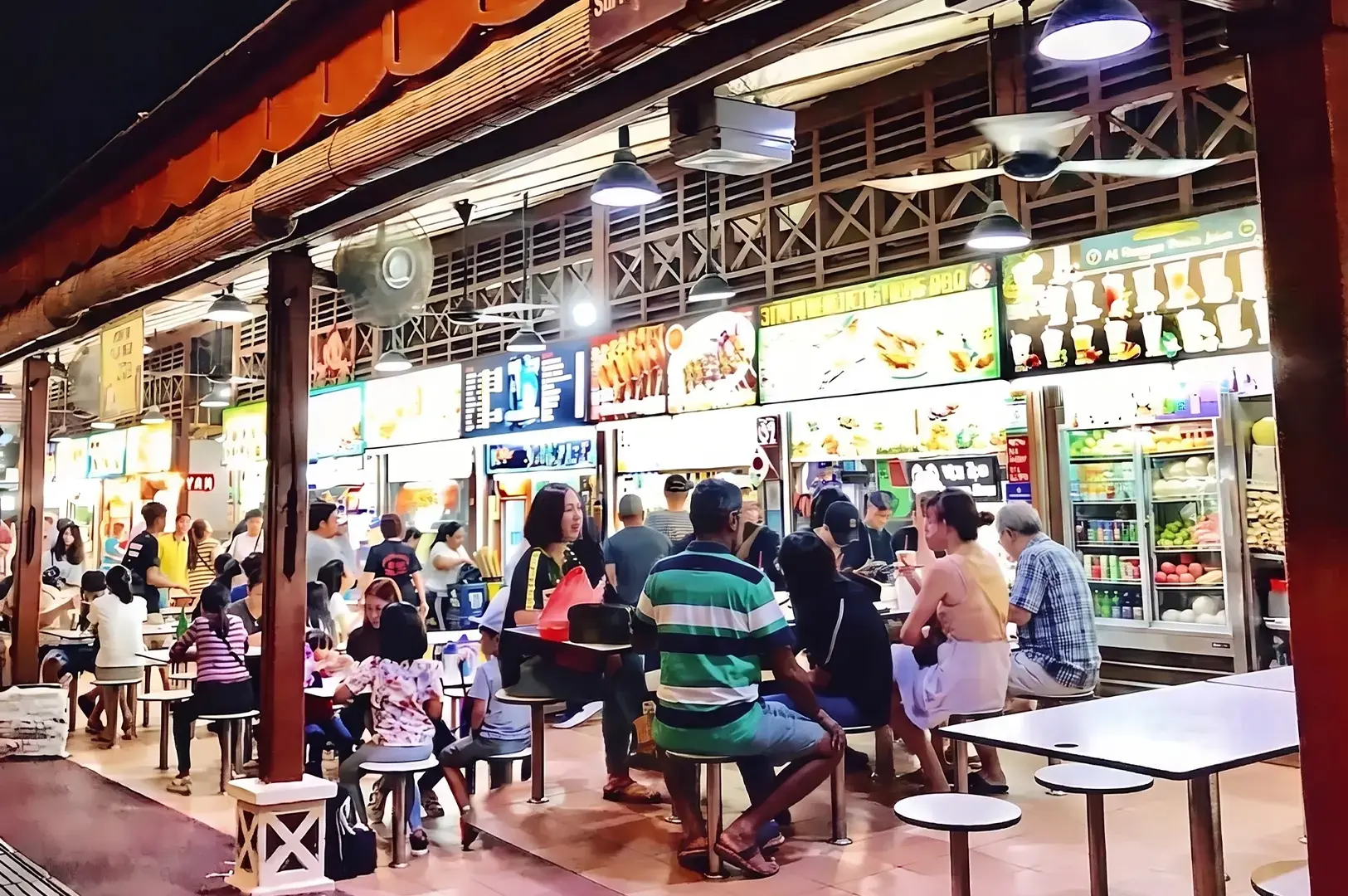A lively nighttime scene of people dining at tables in a brightly lit, open-air hawker center.