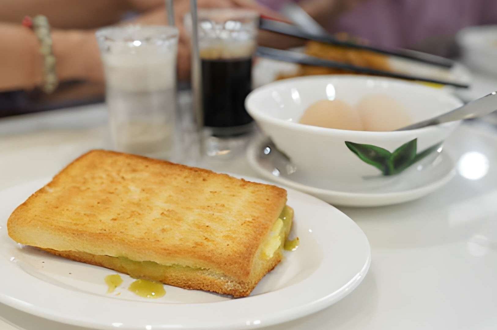 A white plate displaying a Kaya Toast sandwich, highlighting its crispy exterior and rich coconut jam filling.