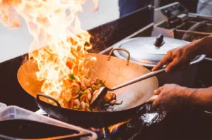 A chef stir-frying fresh vegetables in a large wok over a high-intensity flame, showcasing the traditional wok hei cooking technique.