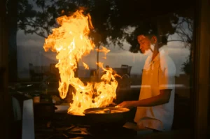 A chef expertly stir-frying in a wok over a high-heat flame, showcasing the "wok hei" technique during a sunset outdoor cooking session.