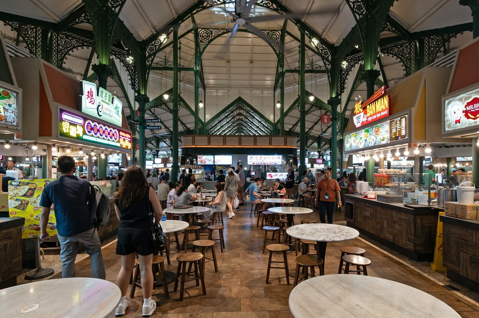 An expansive indoor hawker market in Singapore, filled with tables and chairs for patrons to enjoy their meals.