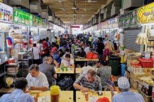 Diners seated at tables in a lively food court at Tekka Centre, Little India, Singapore, surrounded by a vibrant atmosphere. Photo by Johor Kaki.