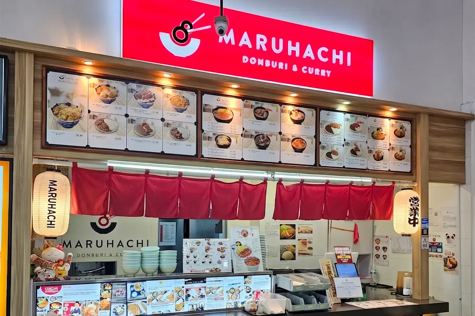 Maruhachi Donburi & Curry Japanese food stall storefront with a red illuminated sign, menu board, and counter.