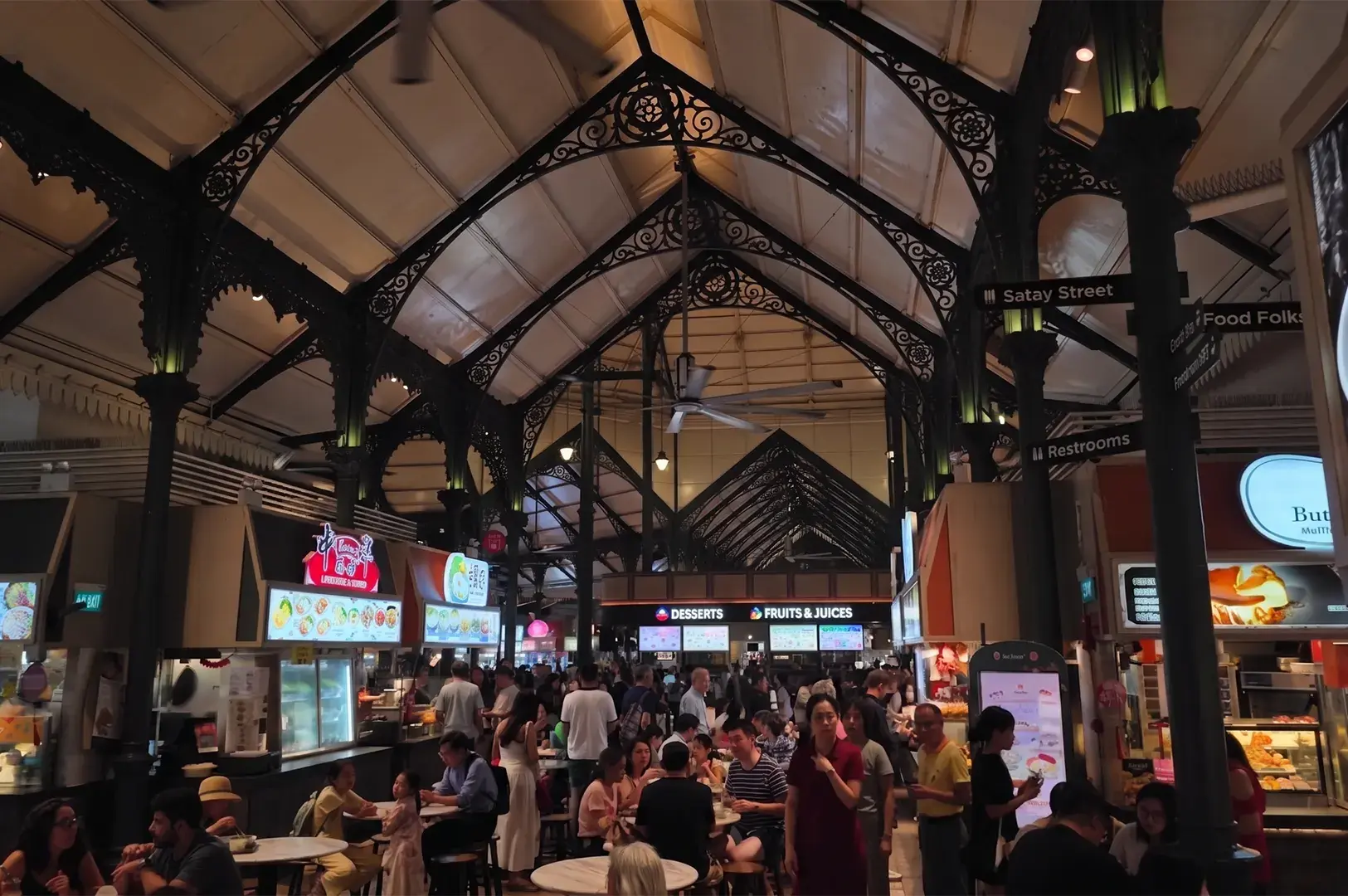 Busy interior of the historic Lau Pa Sat hawker center in Singapore featuring Victorian-style ironwork arches, food stalls, and people dining.