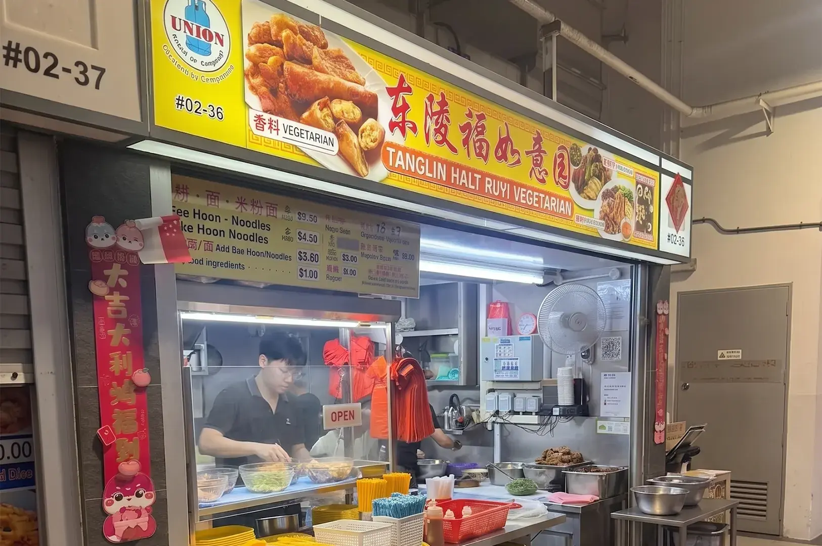 Tanglin Halt Ruyi Vegetarian hawker stall in Singapore featuring a vendor preparing noodle dishes behind a food counter.