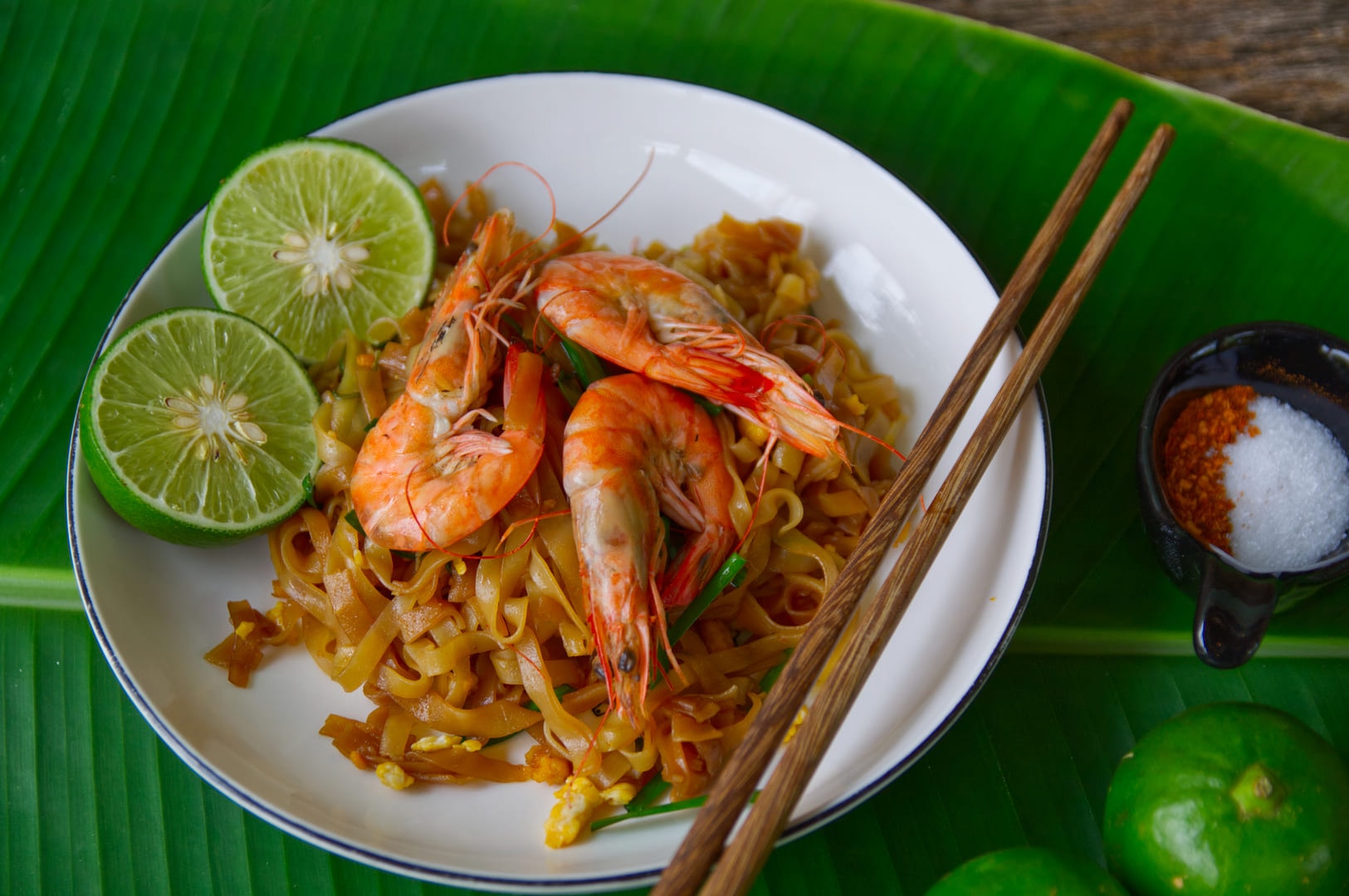 A plate of Char Kway Teow with shrimp, noodles, lime and chopsticks, showcasing Tiong Bahru's culinary offering.