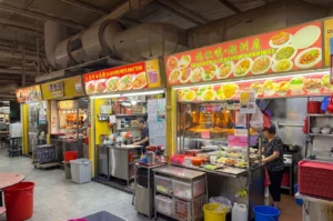 Row of traditional hawker center food stalls in Singapore featuring Teochew porridge and fried kway teow.