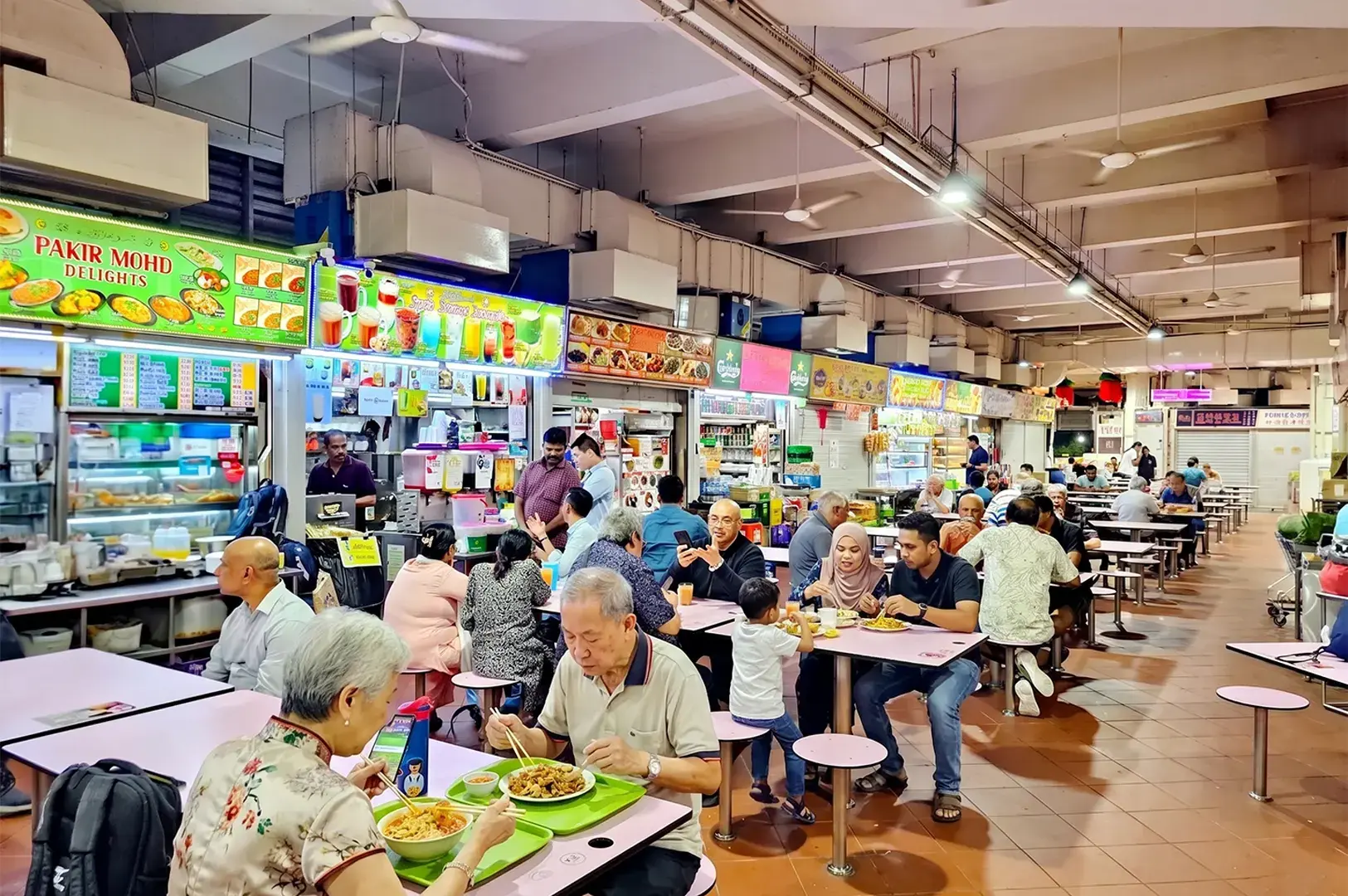 Diners enjoying local food at the Tekka Centre hawker market in Little India, Singapore, featuring Pakir Mohd Delights stall.