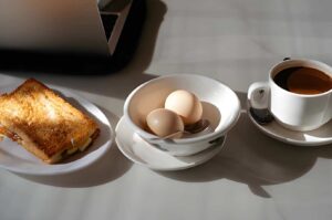 A serving of Kaya Toast accompanied by eggs and tea, arranged neatly on a white plate for breakfast.