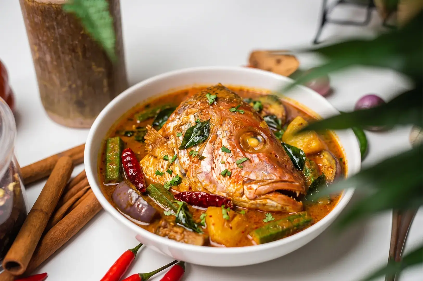 Spicy fish head curry served in a black clay pot with okra and eggplant.
