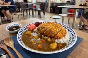 A plate of Japanese katsu curry on a table in a bustling food court.