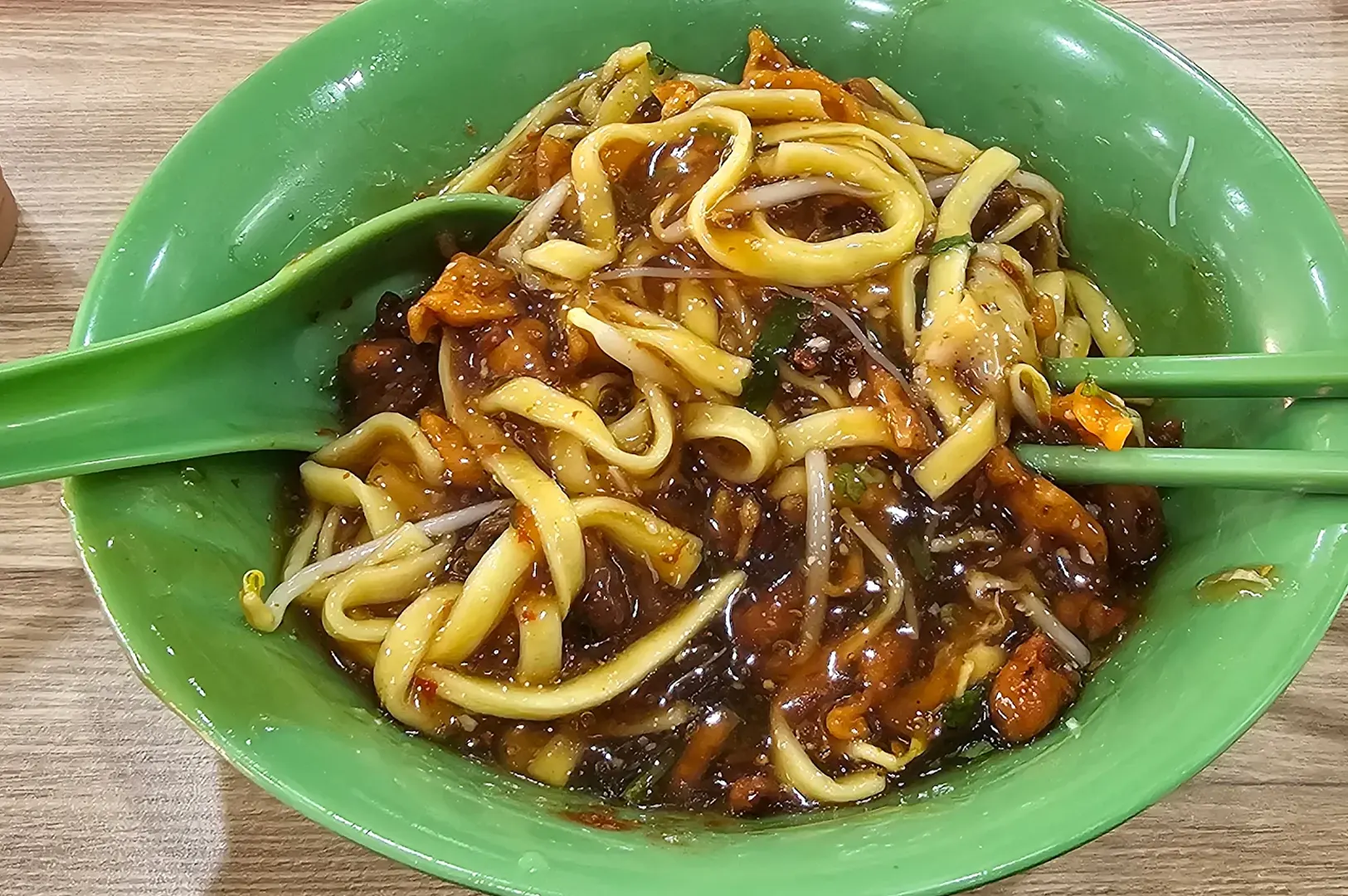 A bowl of Lor Mee flat yellow noodles in a thick, dark savory gravy with bean sprouts.