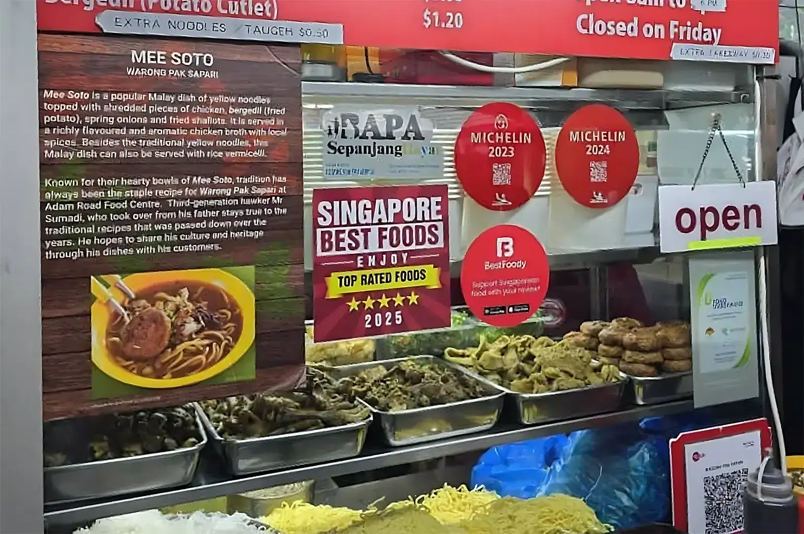 A close-up of a hawker stall food counter displaying ingredients, Michelin Bib Gourmand stickers, and an information board describing traditional Mee Soto.