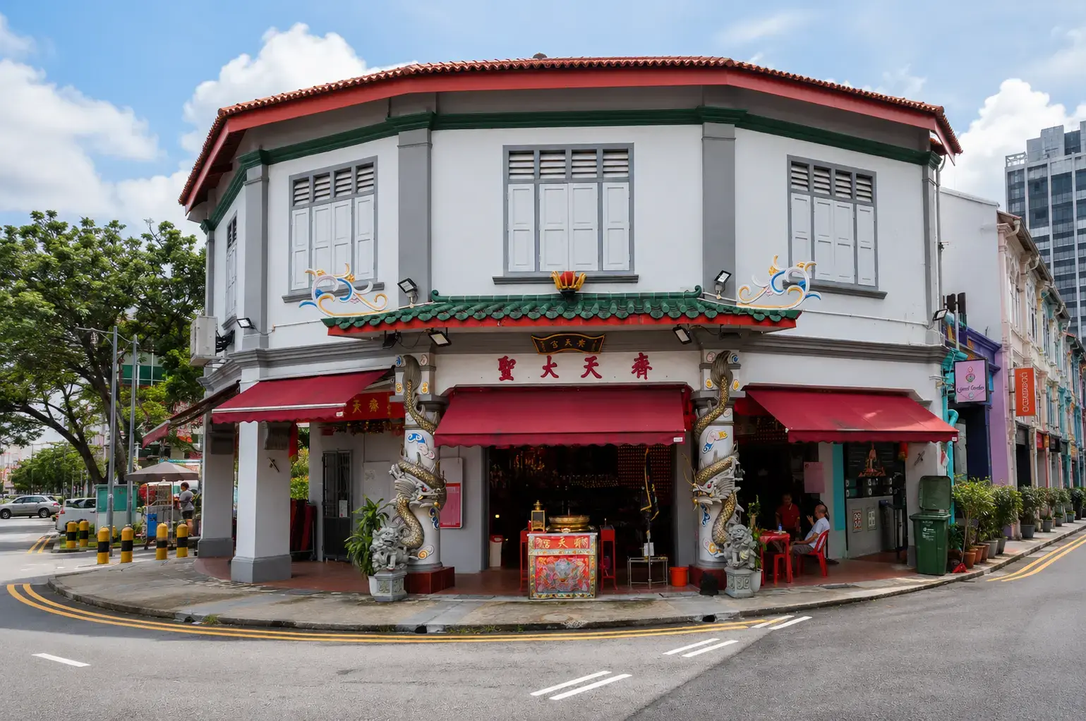 A two-story, corner heritage shophouse featuring a Chinese temple on the ground floor, adorned with ornate dragon pillars, red awnings, and Chinese characters on the facade.